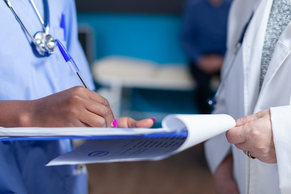 Close up of nurse signing files wtih help from doctor in healthcare cabinet A close-up of a nurse and doctor completing medical documentation on a clipboard